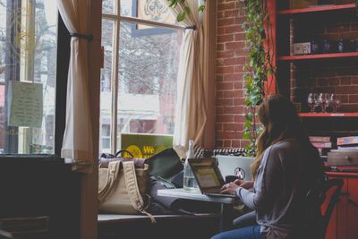 young woman working on her laptop sitting by a window in a cafe
